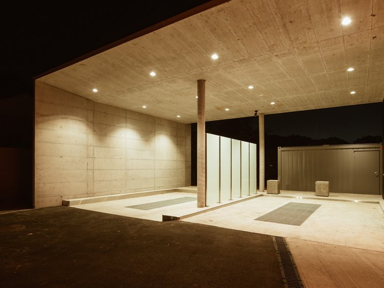 Die Vorderansicht einer beleuchteten Tankstelle mit Zapfsäulen, Shop und Abstellplätzen bei Nacht.